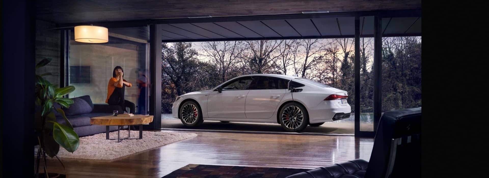 Luxury car parked outside modern glass-walled living room, featuring stylish decor and forest view.