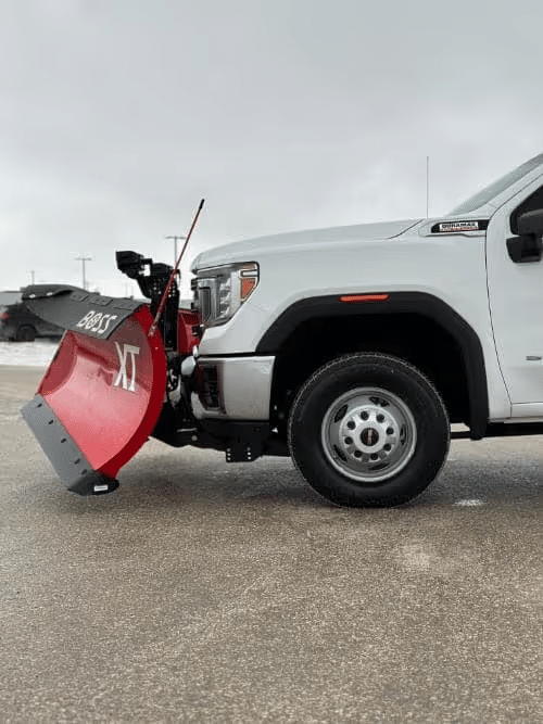 White pickup truck with red Boss XT snow plow attached, parked on a snowy road.