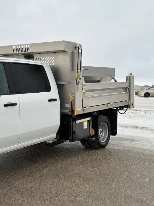 White pickup truck with a metallic dump bed attachment on a snowy street.
