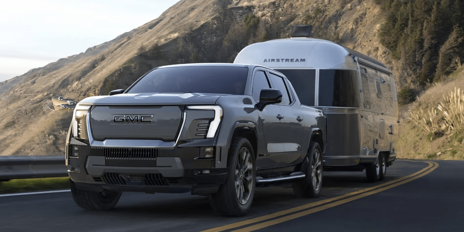 GMC truck towing an Airstream trailer on a scenic mountain road.