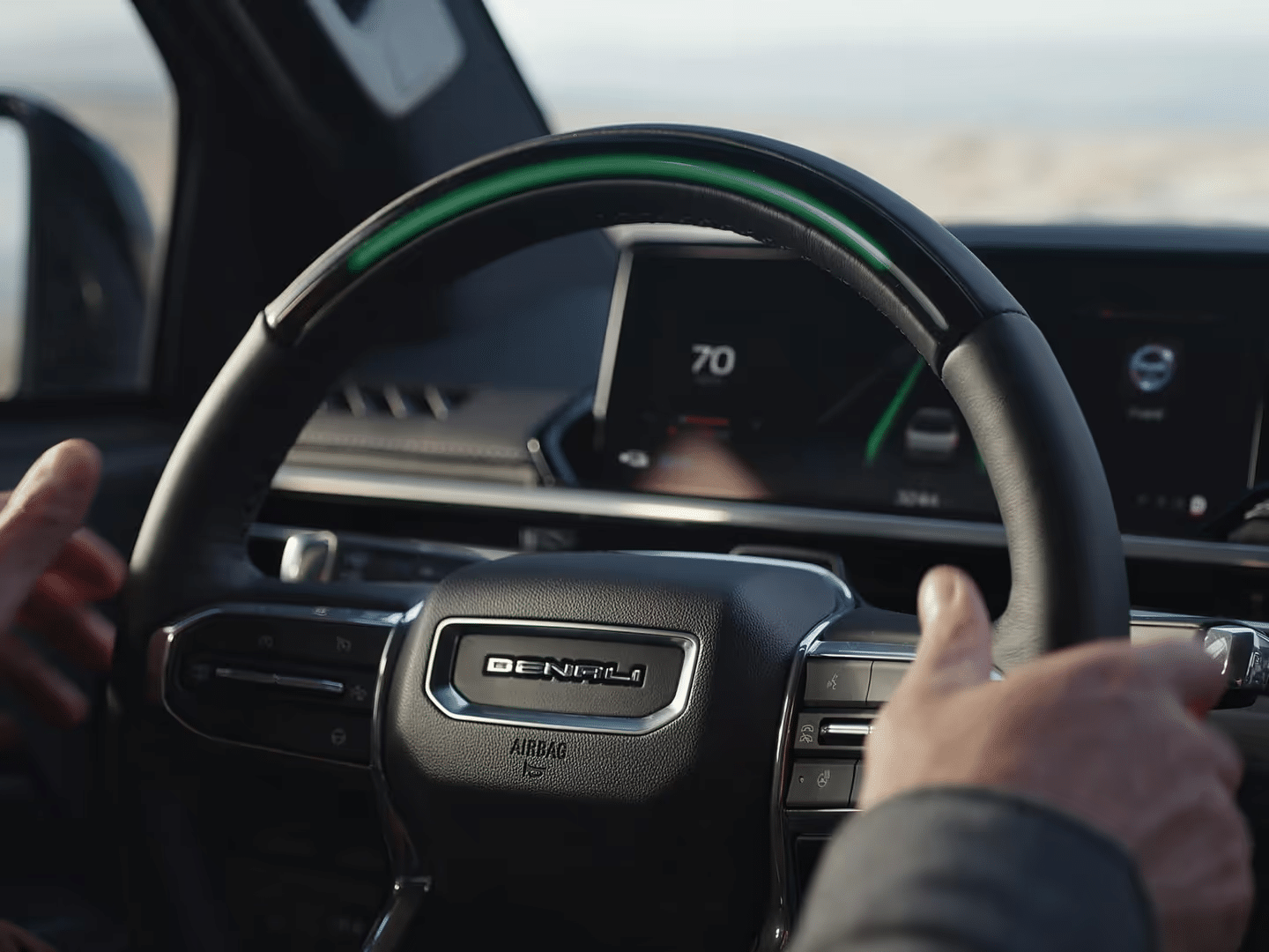 Driver's hands on luxury car steering wheel with digital dashboard displaying speed.
