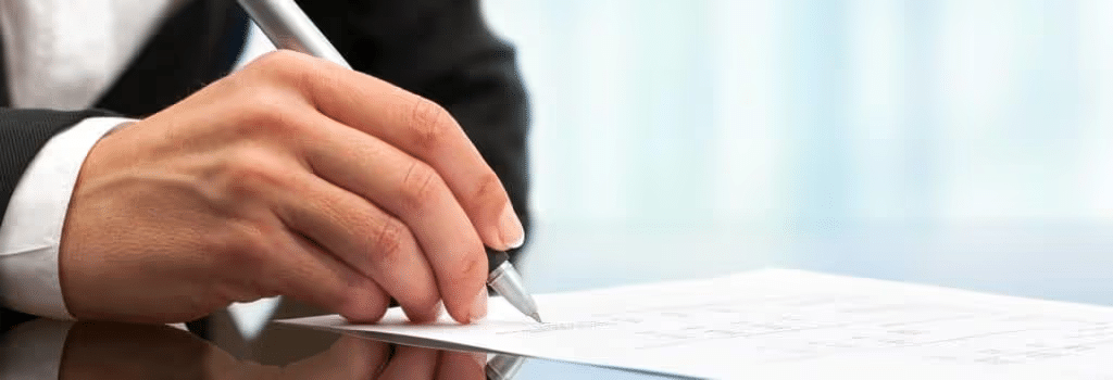 Businessperson signing a document with a pen, signifying agreement and professionalism.