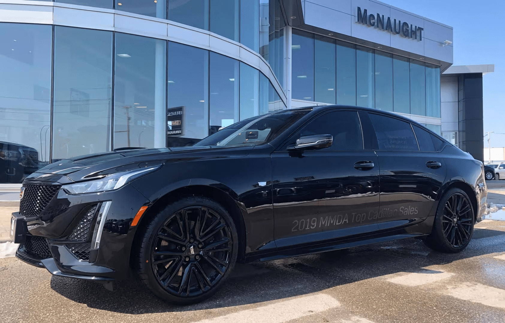 Sleek black Cadillac sedan parked outside a modern dealership, showcasing luxury design.