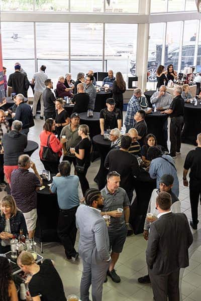 Group of people networking at an indoor event with tables and large windows.