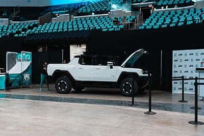 White electric SUV displayed in an indoor venue, surrounded by barriers and seating.