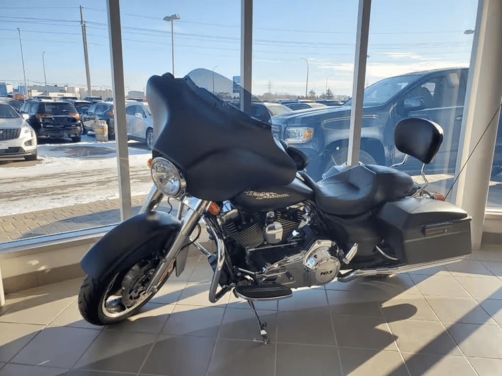 Black touring motorcycle displayed in a sunlit showroom, featuring a large windshield and comfortable seat.
