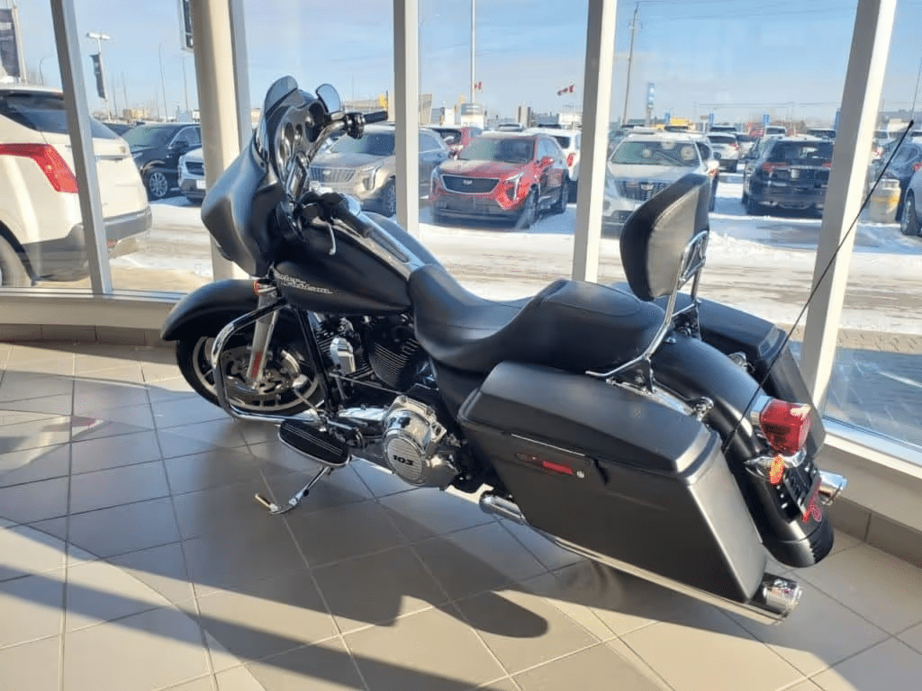 Black touring motorcycle in showroom with large windows revealing parked cars outside.