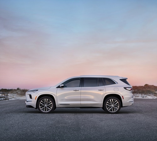 White SUV parked on a beach road at sunset, with pink and blue skies in the background.