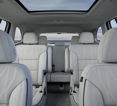 Luxury SUV interior with white leather seats and a panoramic sunroof, offering spacious comfort.