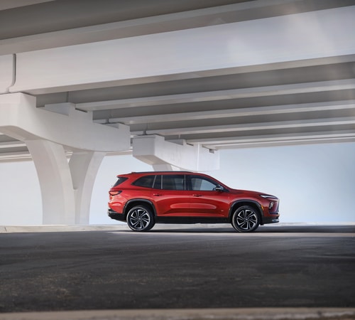 Red SUV parked under a modern highway overpass, highlighting sleek design and urban setting.