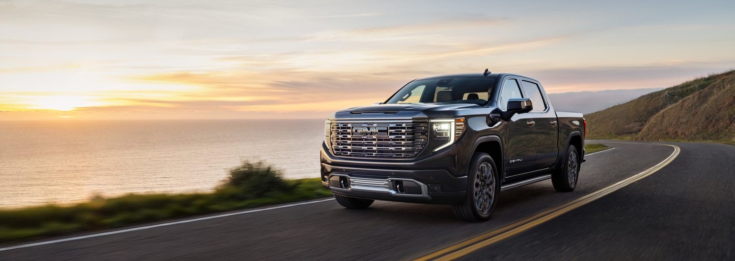A shiny red SUV is parked in a dimly lit urban setting at night. The car features a sleek design with distinctive wheel rims, and illuminated headlights, reflecting light on the wet pavement. Modern architectural elements are visible in the background.