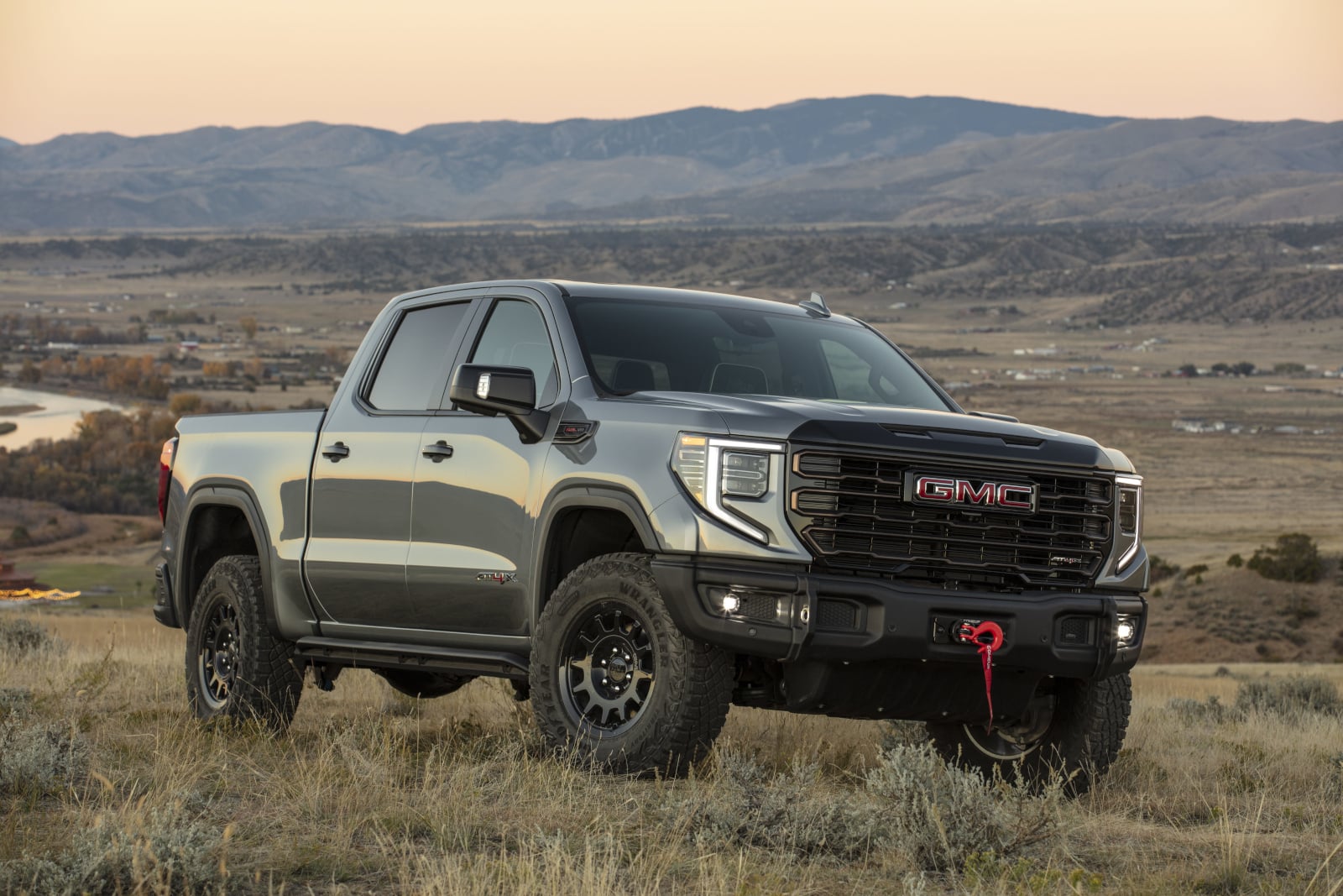 Silver GMC truck parked in a grassy field with mountain range backdrop at sunset.