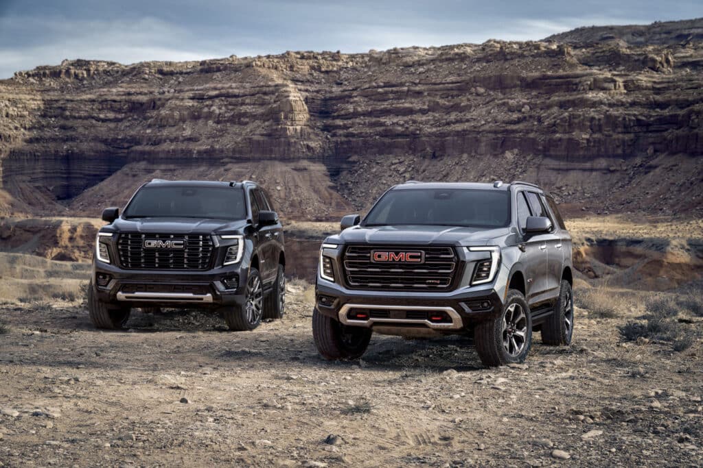 Two GMC SUVs parked in a rugged desert landscape, showcasing their bold design.
