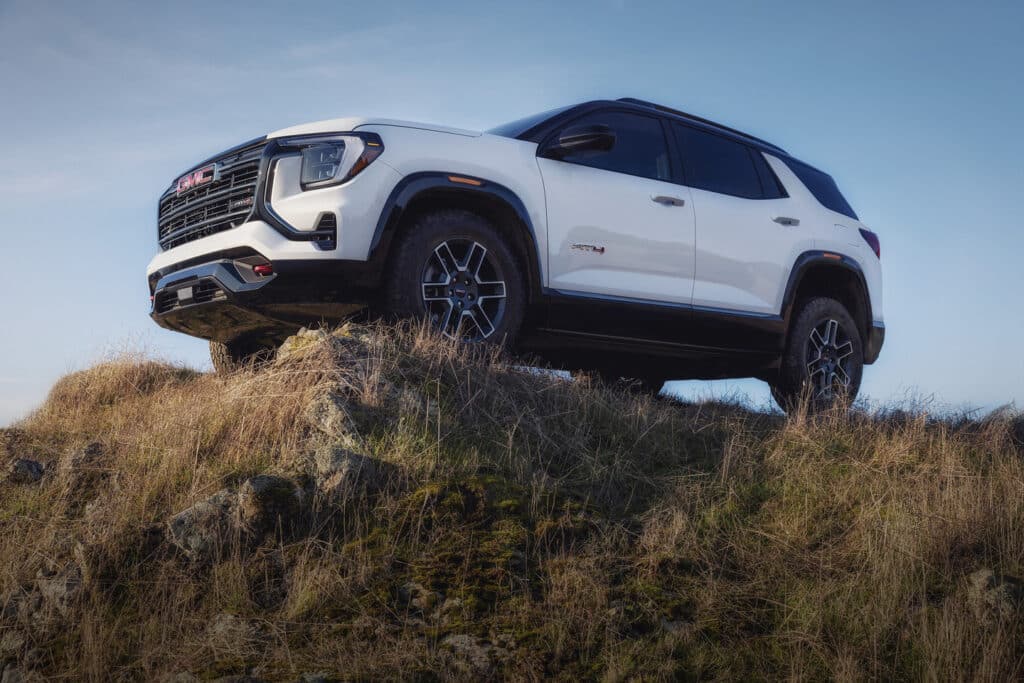 White SUV on a grassy hill under a clear blue sky, showcasing rugged terrain capability.