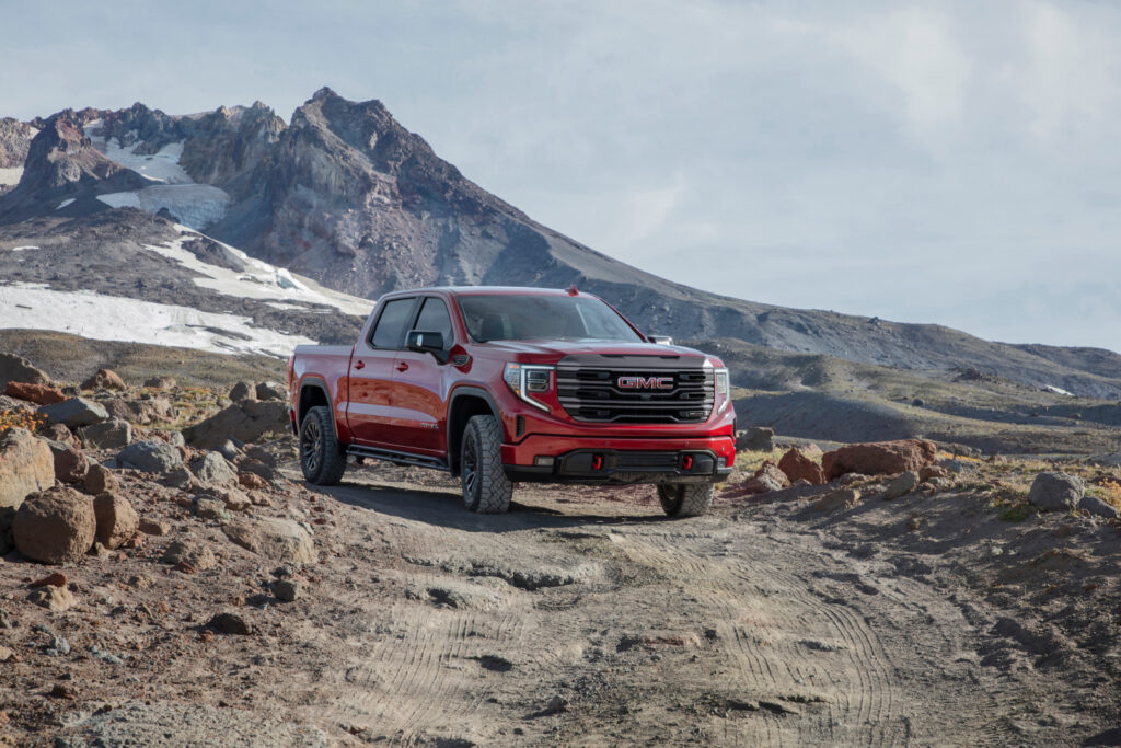Red GMC truck on rocky terrain with mountain background.