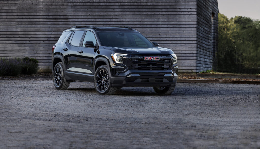 A black SUV parked on gravel in front of a wooden building, featuring modern design and GMC branding.
